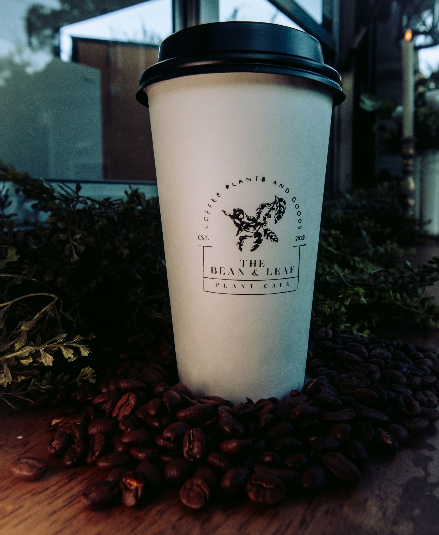 White coffee cup with Bean & Leaf logo surrounded by scattered coffee beans in warm lighting.