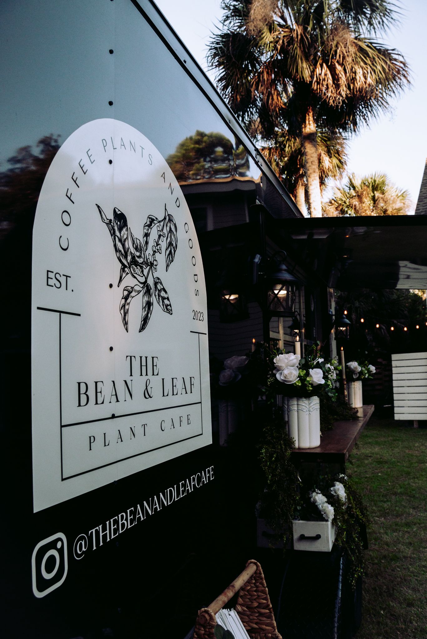The Bean & Leaf Plant Cafe logo displayed on a black mobile coffee cart under palm trees.