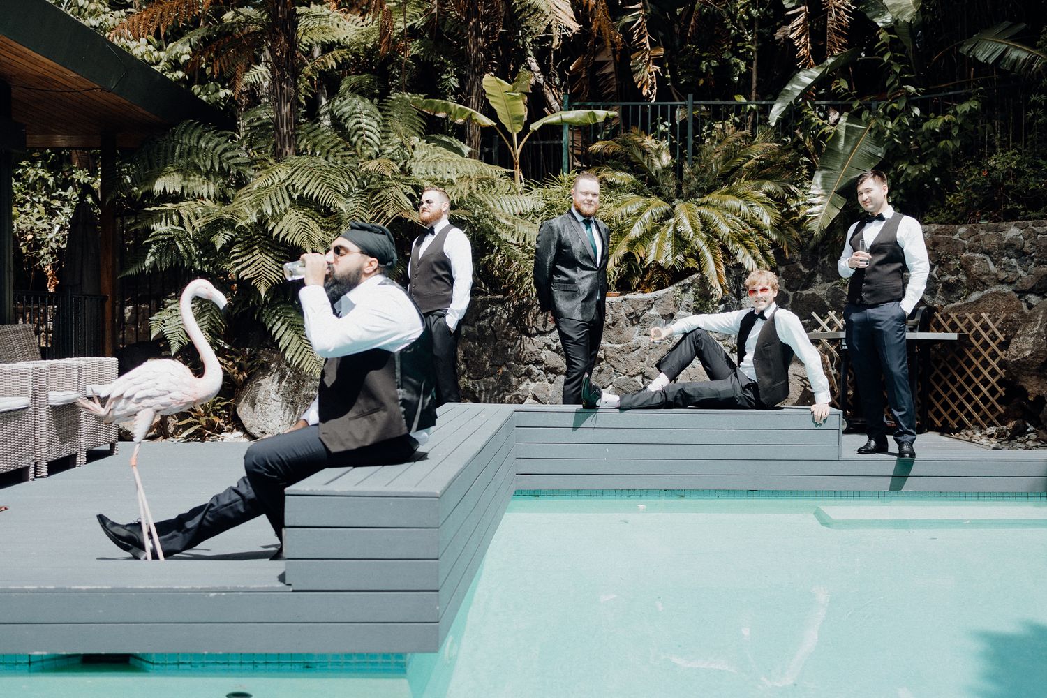 The Groom'smen and the groom pose creatively on a gray deck, captured by Apertured Media Auckland Wedding Photographer.