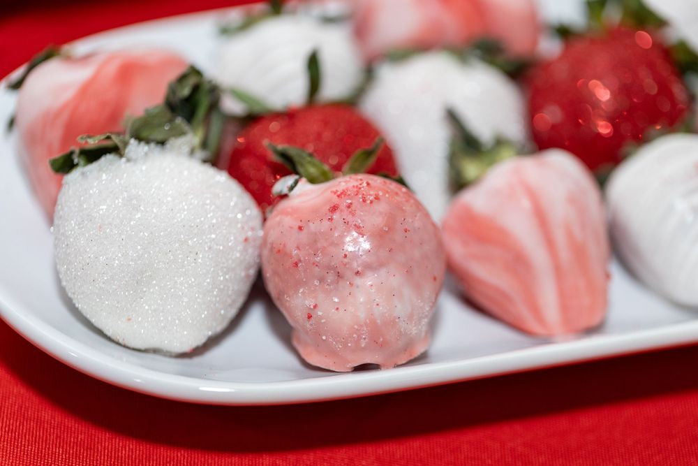 White and pink chocolate covered strawberries served on a white plate with red accent.