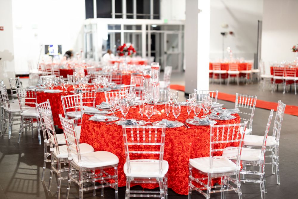 Elegant red and white party table settings with silver Chiavari chairs in a modern event space.