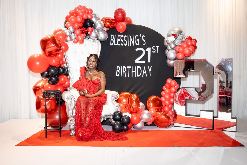 A birthday celebration backdrop with red and black balloon decorations and '21st Birthday' signage.