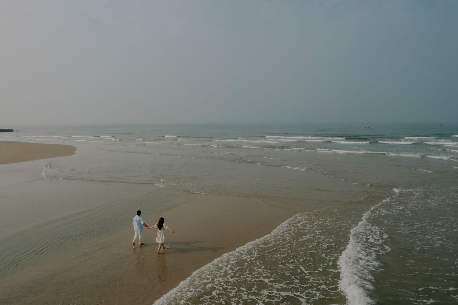 A silhouetted couple stands on a beach at sunset holding sparklers against the purple sky.