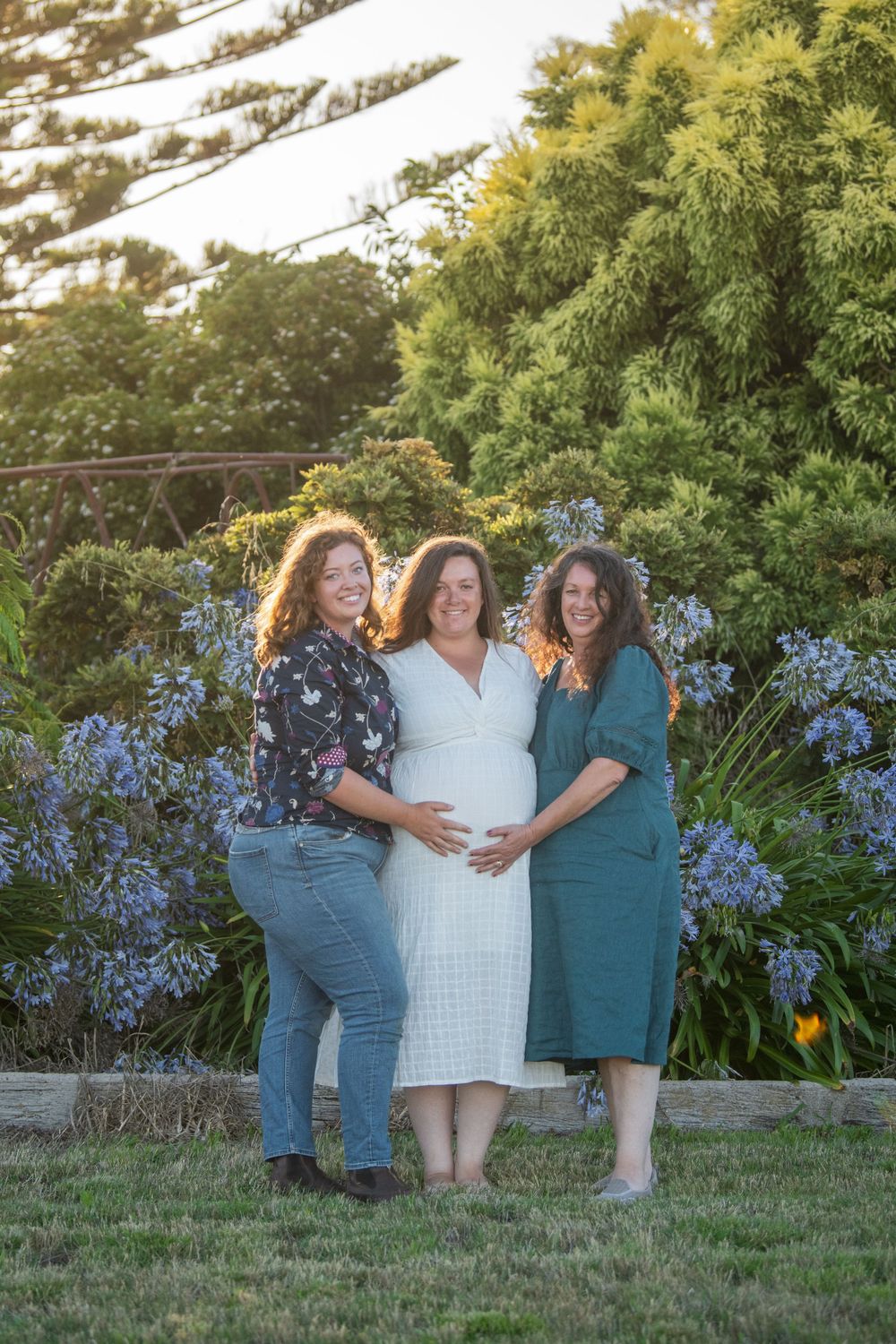Three people standing together in a garden with beautiful blue flowers and greenery in the background.