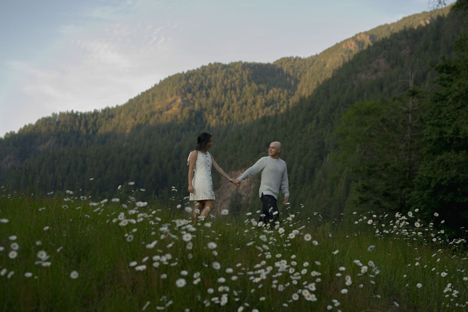 Two figures stand in a mountain meadow filled with white wildflowers at sunset.