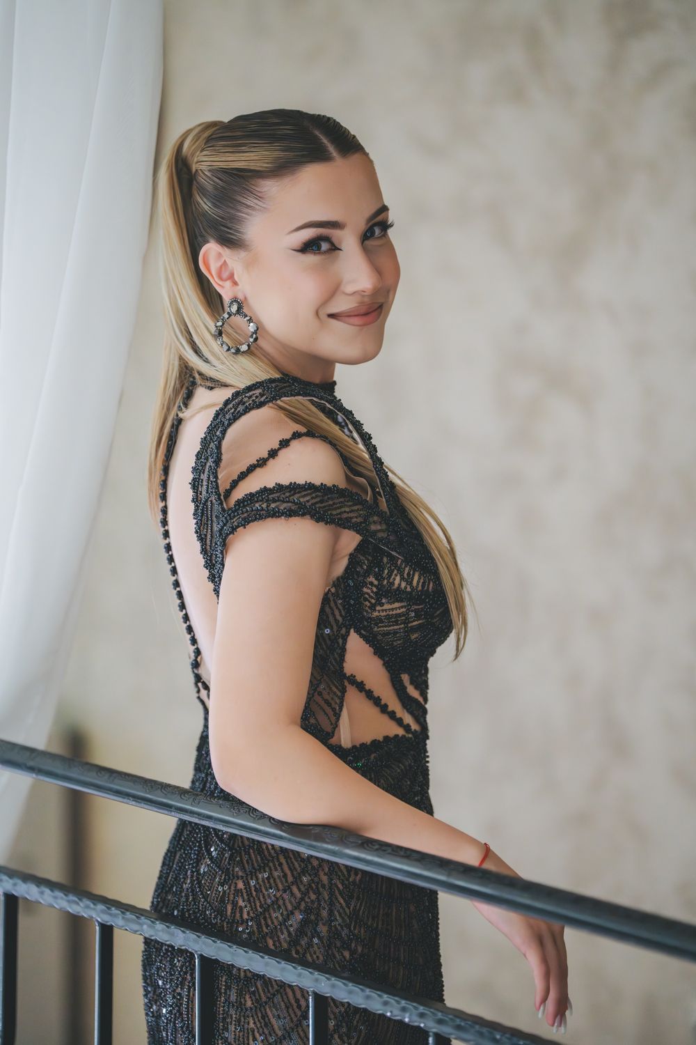 Elegant portrait in black lace dress with statement earrings against light background.