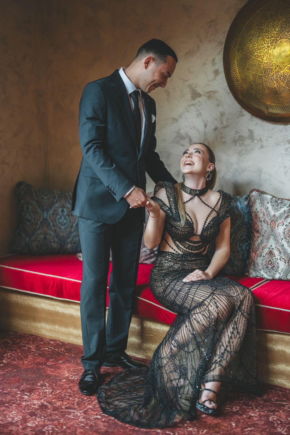 Couple shares romantic moment on vintage sofa, dressed in formal attire under golden wall art.