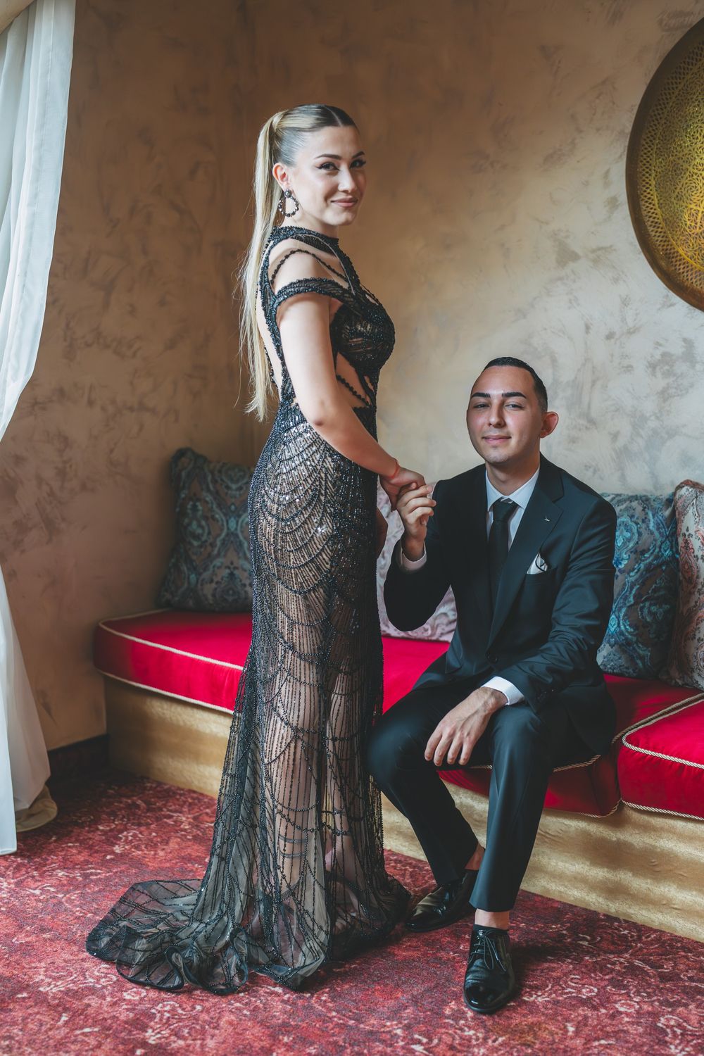 Intimate portrait showing couple in evening wear posing together against textured wall with golden decor.