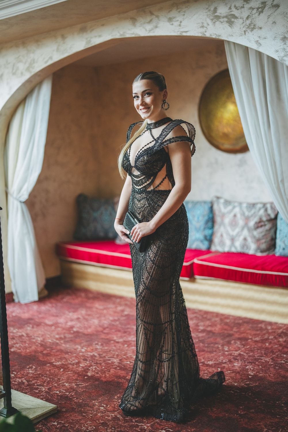 Portrait in arched doorway showing elegant pose in fitted black lace gown with red bench accent.