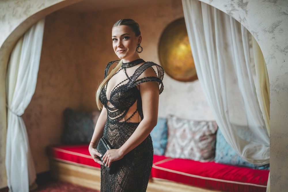Close-up portrait featuring intricate black evening gown with sheer details against neutral backdrop.