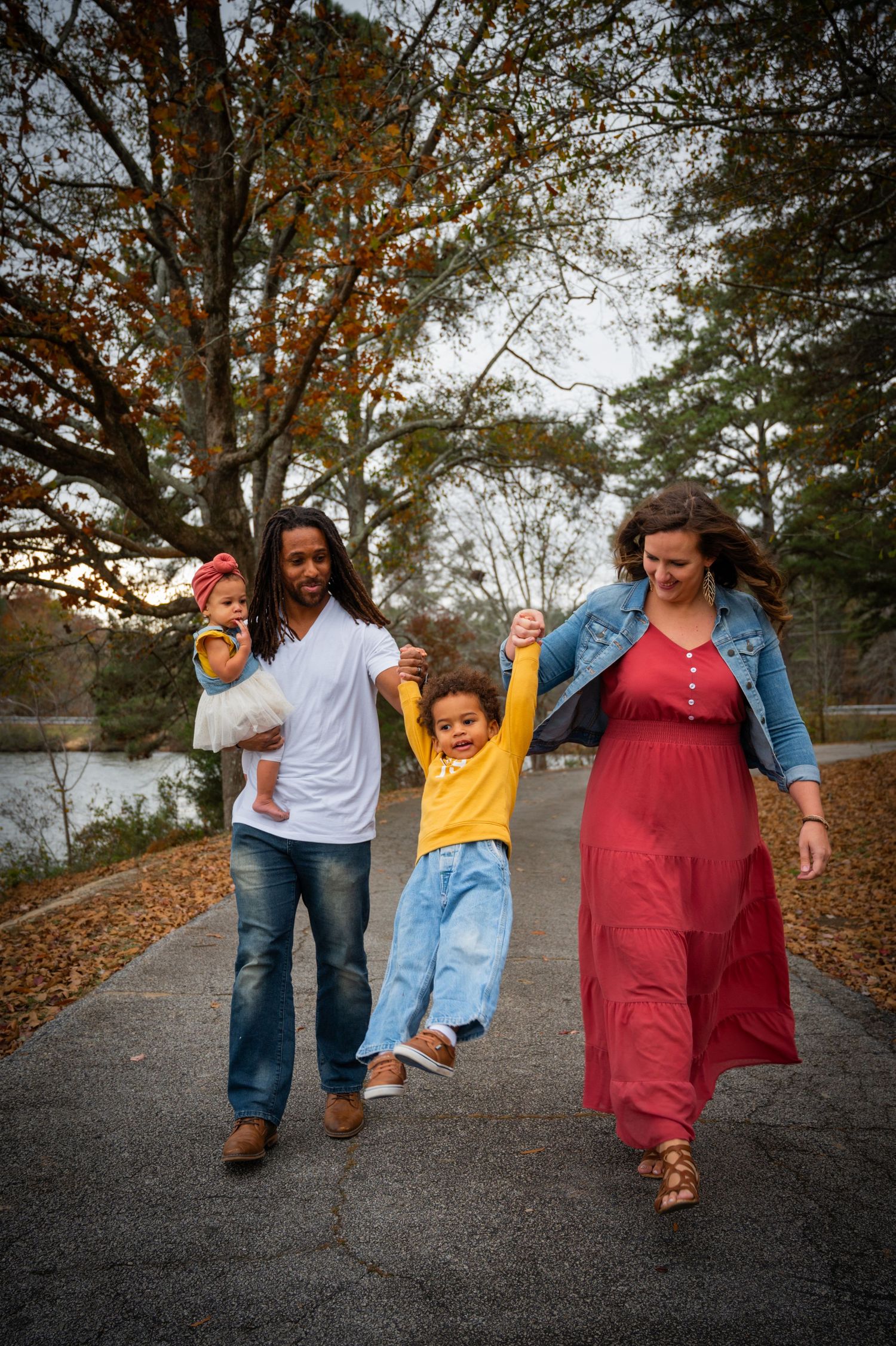 Family walking together on leaf-covered path during fall season.