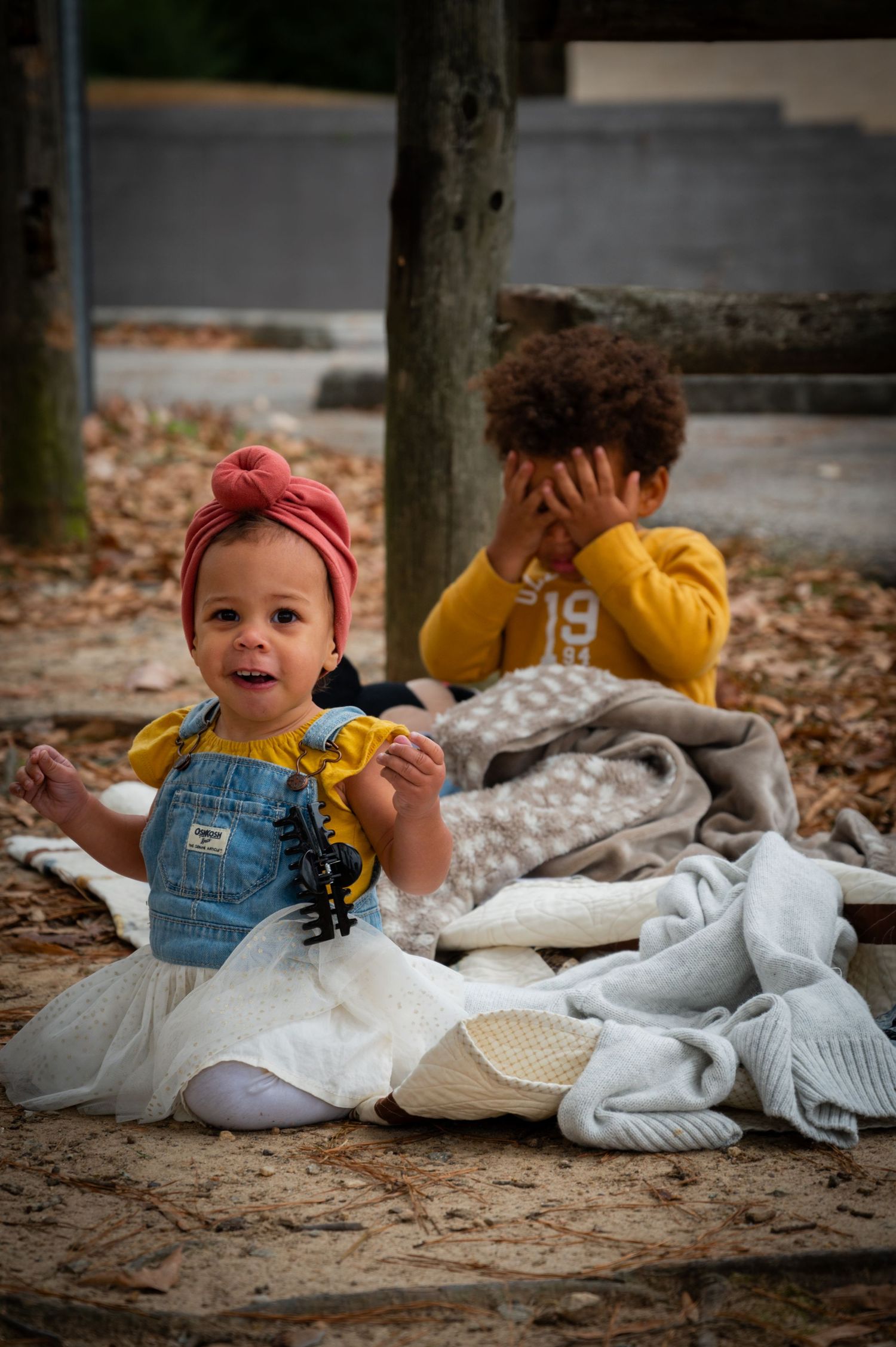 Playful baby in denim and red bow lies on blanket during outdoor photoshoot.