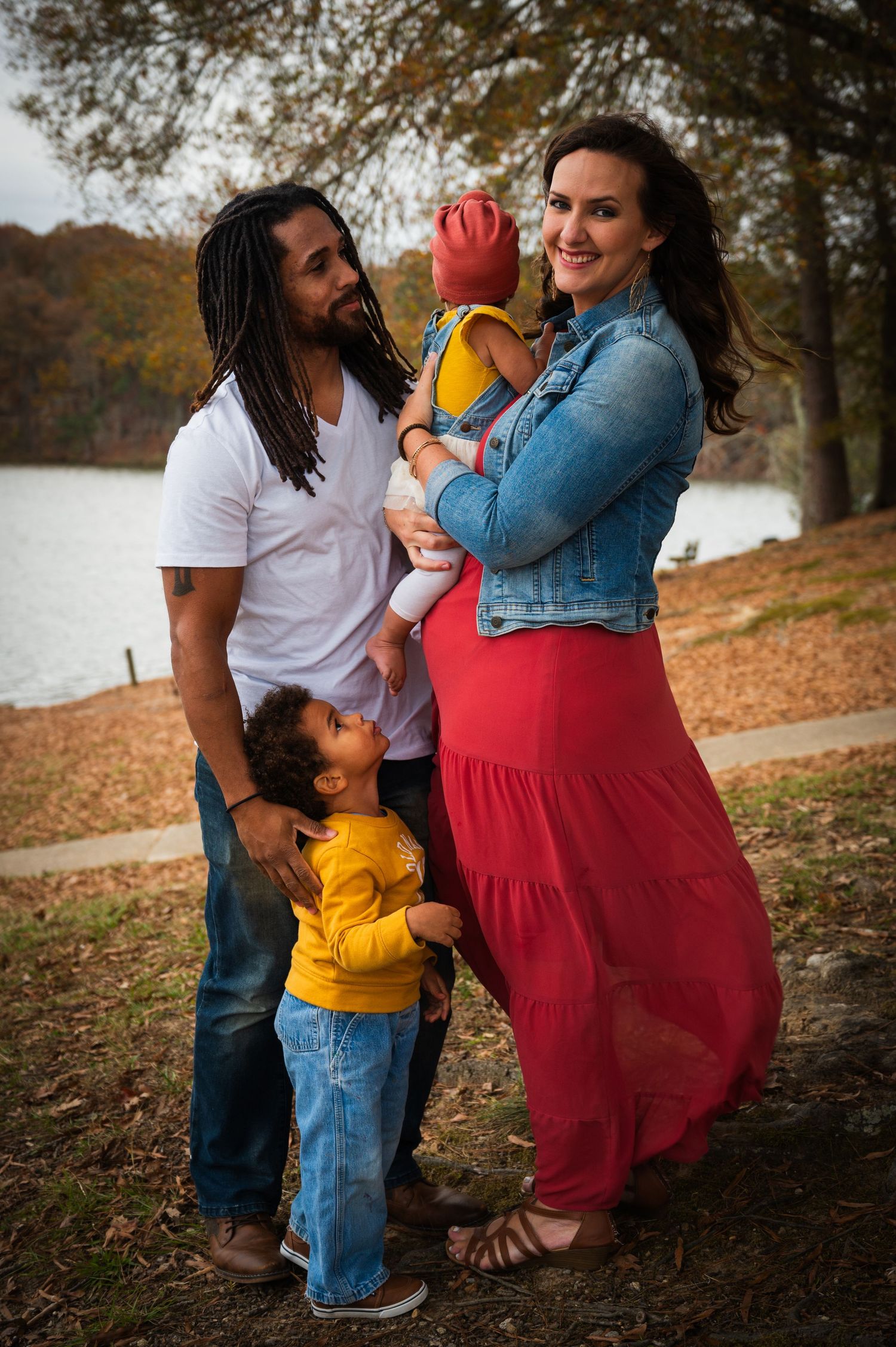 Family shares joyful moment together during outdoor fall photoshoot near water.