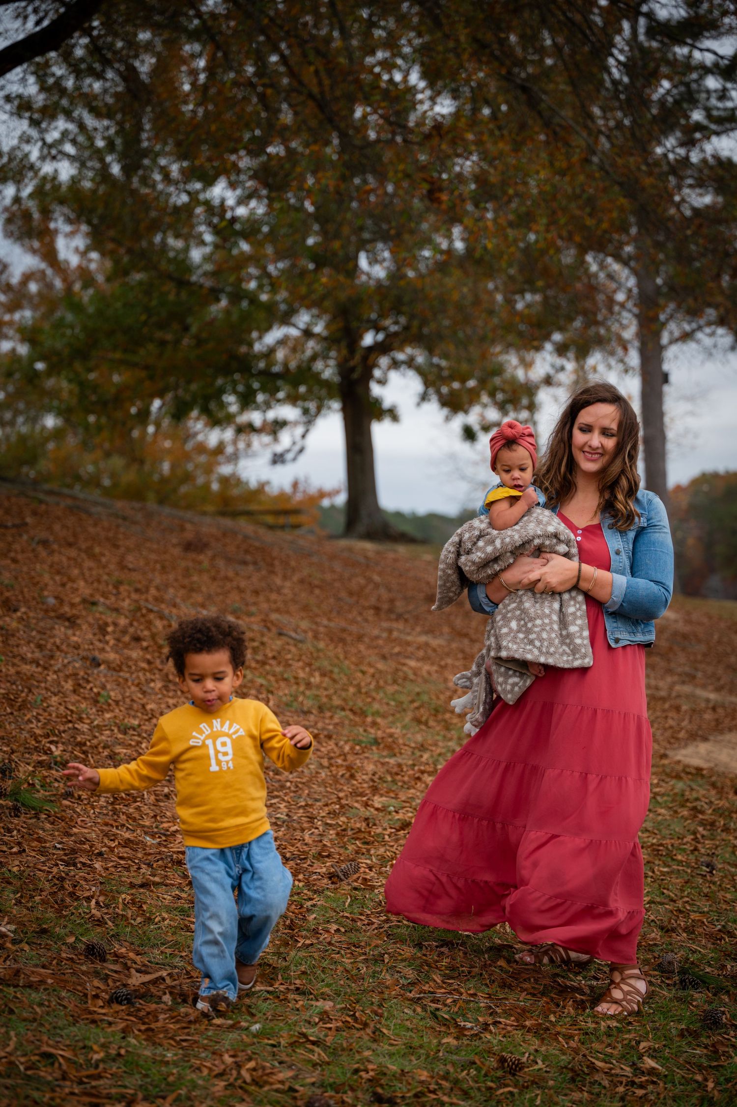 Children explore fall landscape while family takes photos on leaf-covered hill.