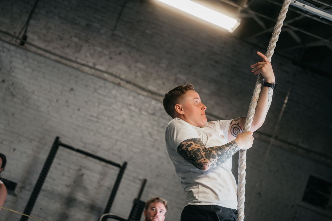 Person performing a rope climb exercise in an industrial gym with white brick walls.