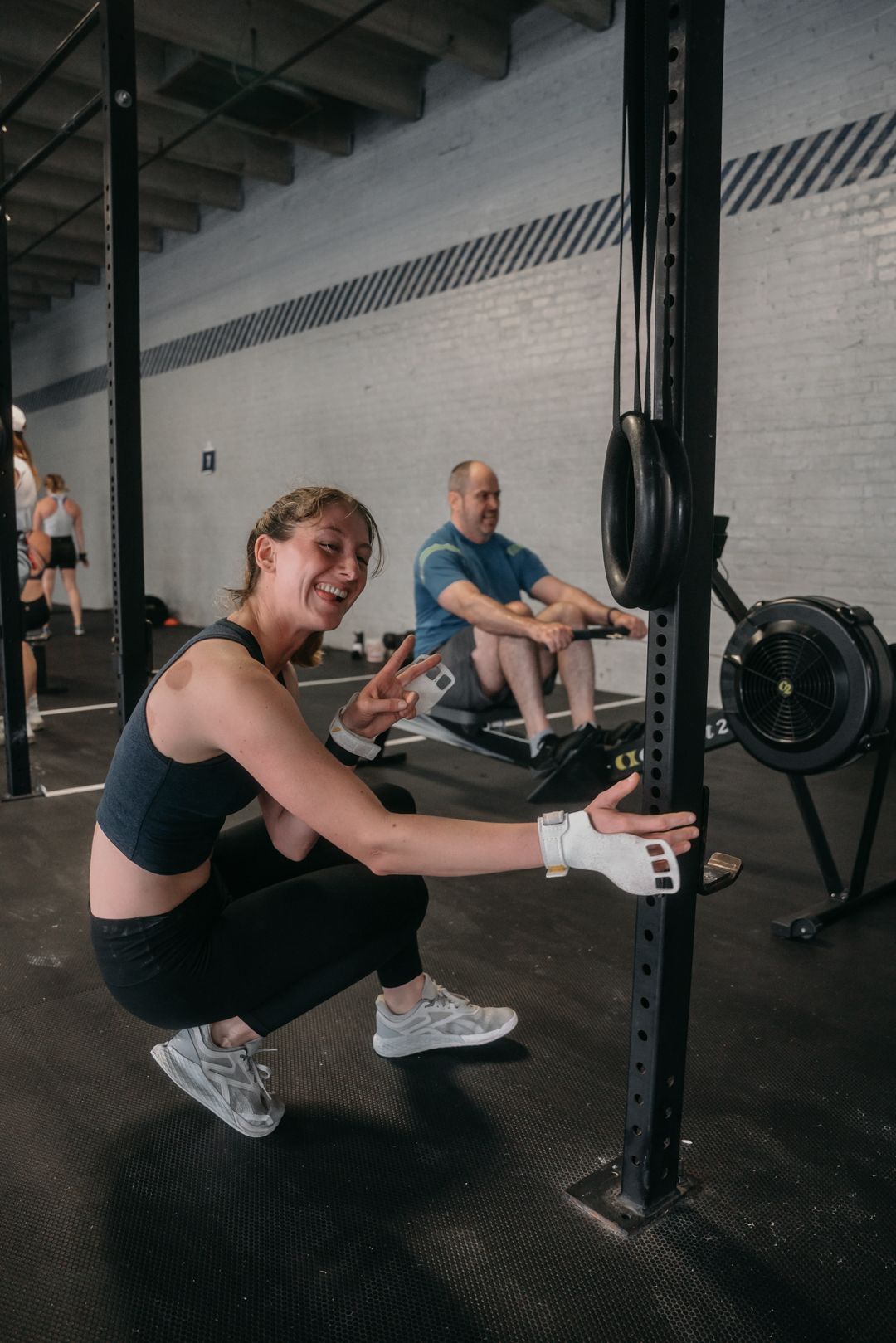 Athlete in workout gear adjusting equipment on a gym rack while others exercise in background.