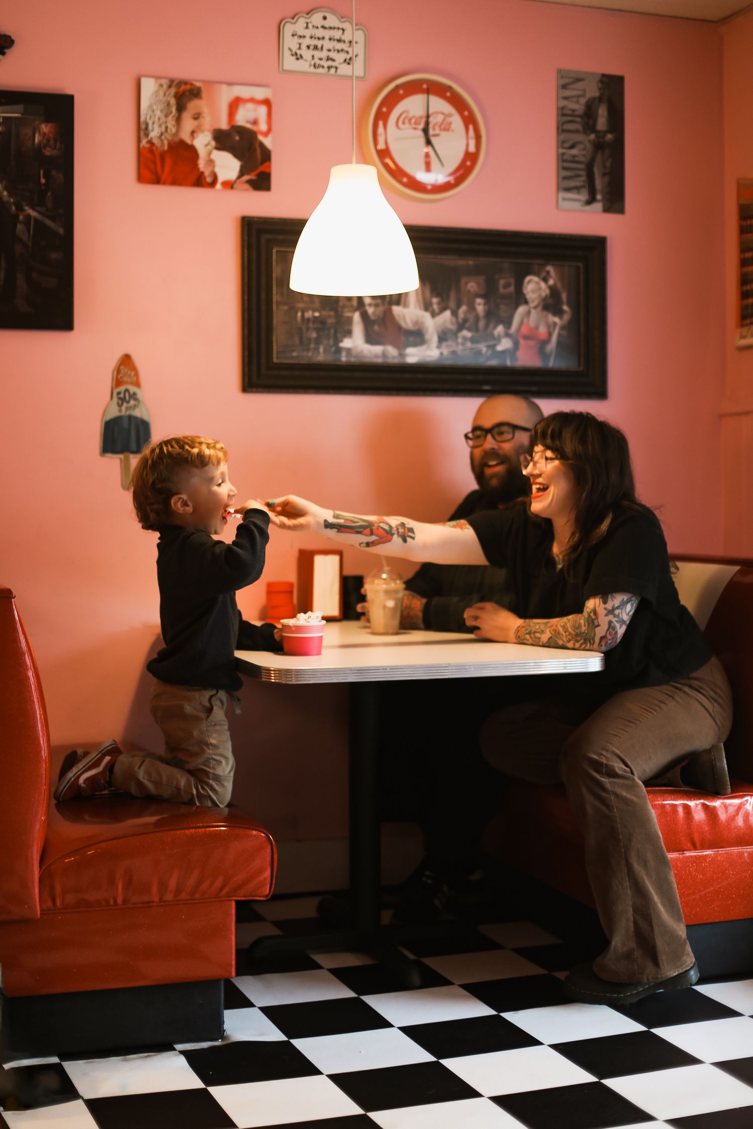 Family dining at retro diner booth with checkerboard floor and pink walls.