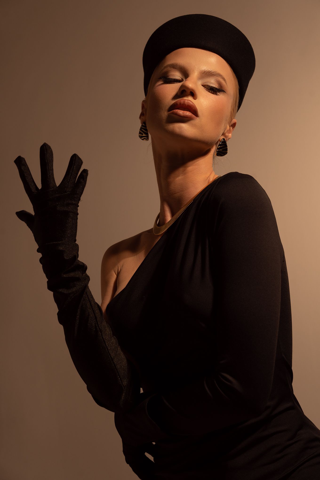 Artistic portrait of someone wearing black clothing and beret against brown background with dramatic shadow and moody lighting.