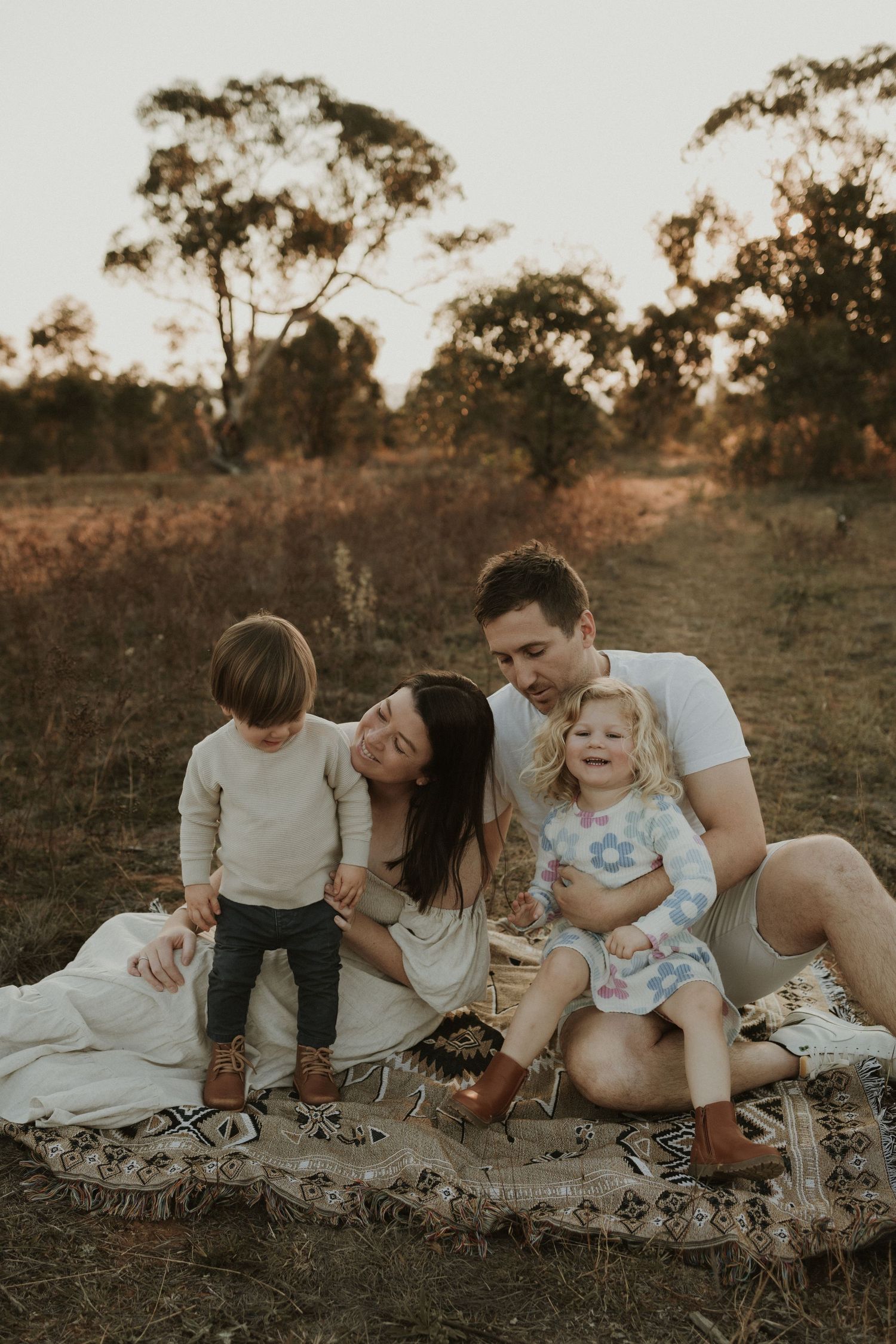 A loving family enjoying a sunset moment together while sitting outside in a Queanbeyan field