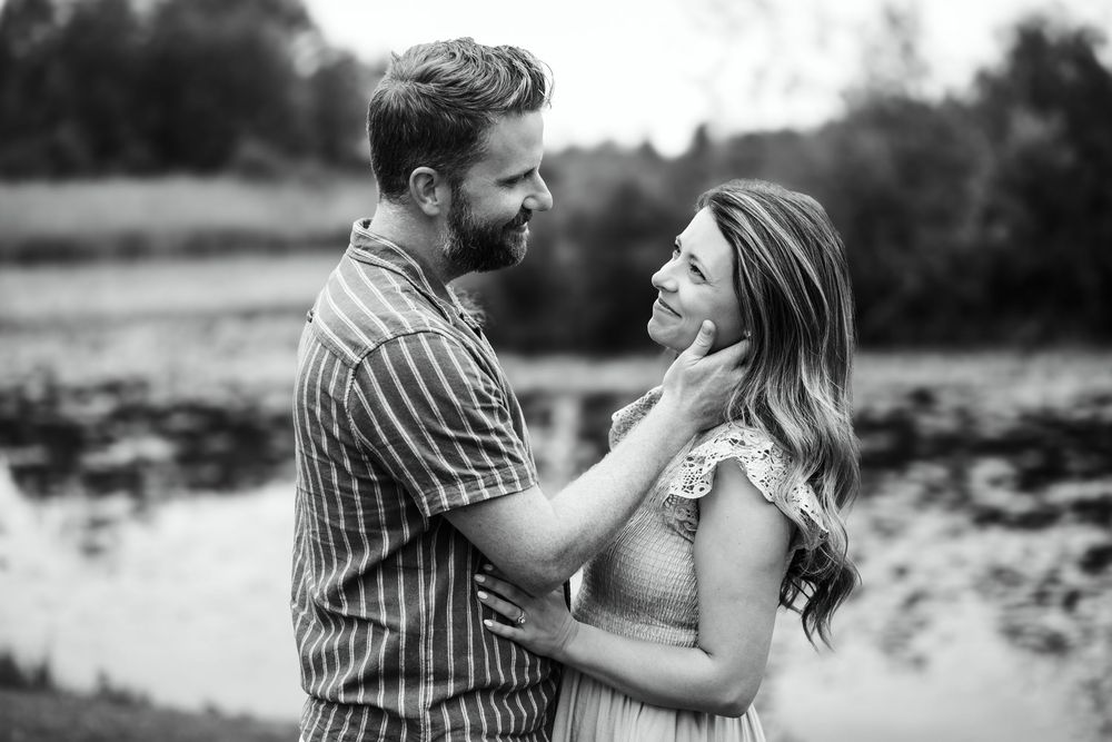 Black and white romantic portrait of couple embracing by a lake.