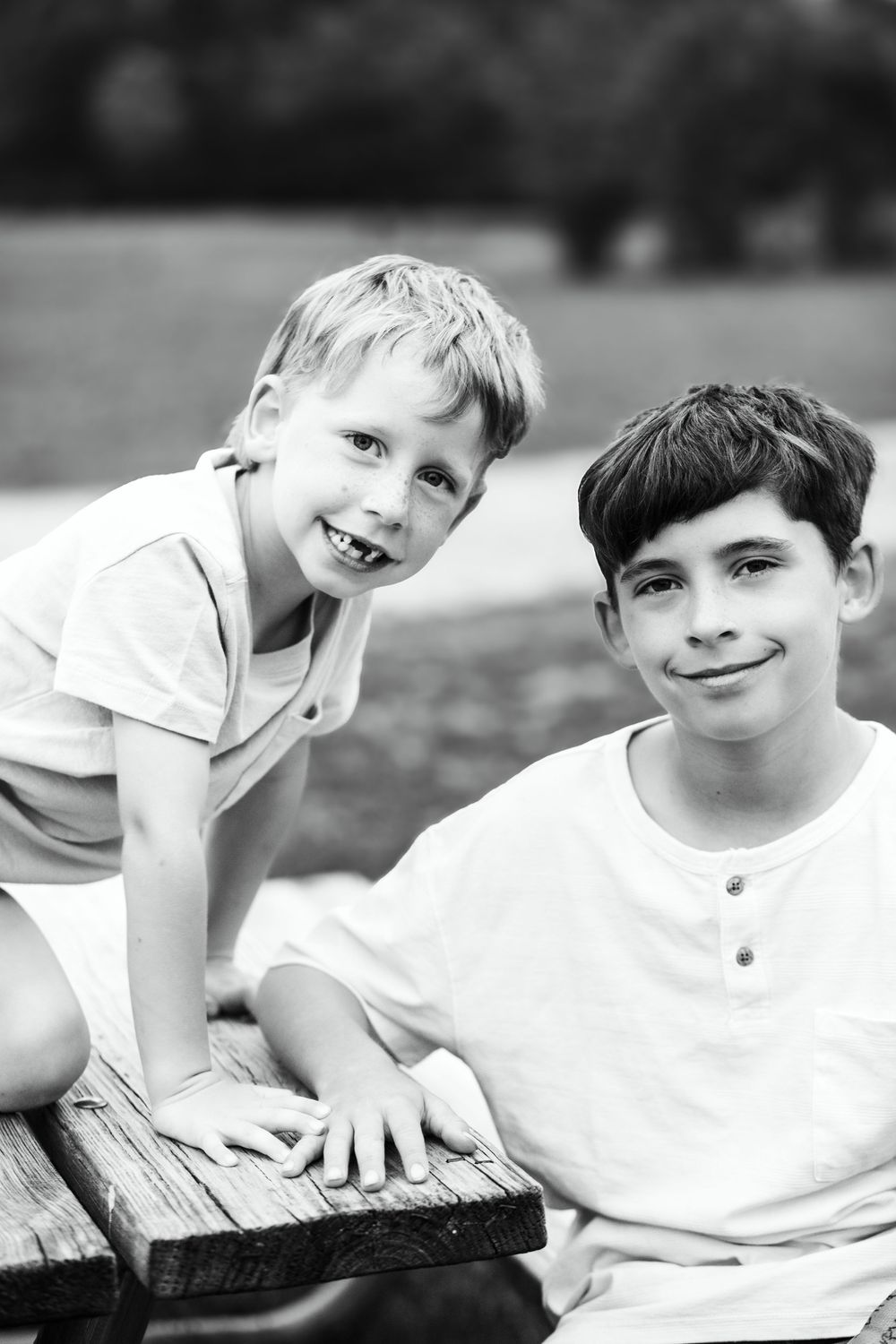 Black and white portrait of two boys sitting on wooden surface outdoors.
