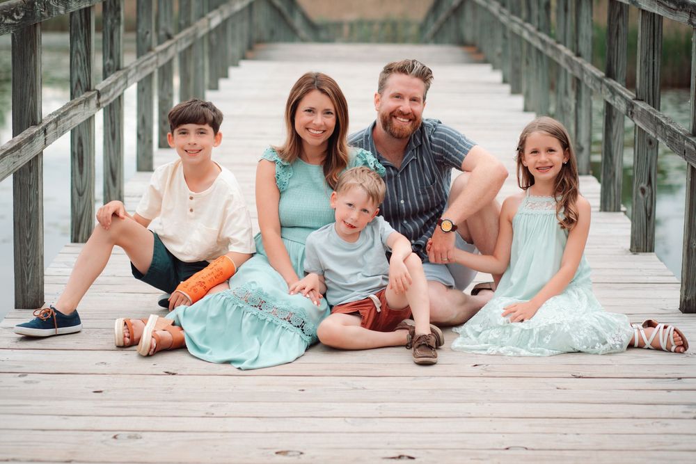 Family lying together on a wooden boardwalk surrounded by greenery in coordinated mint and navy outfits.
