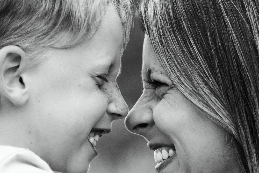 Close up black and white portrait of mother and child touching noses while smiling.