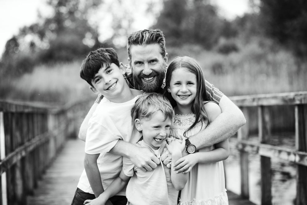 Black and white portrait of a happy family sharing a joyful moment on a wooden bridge.
