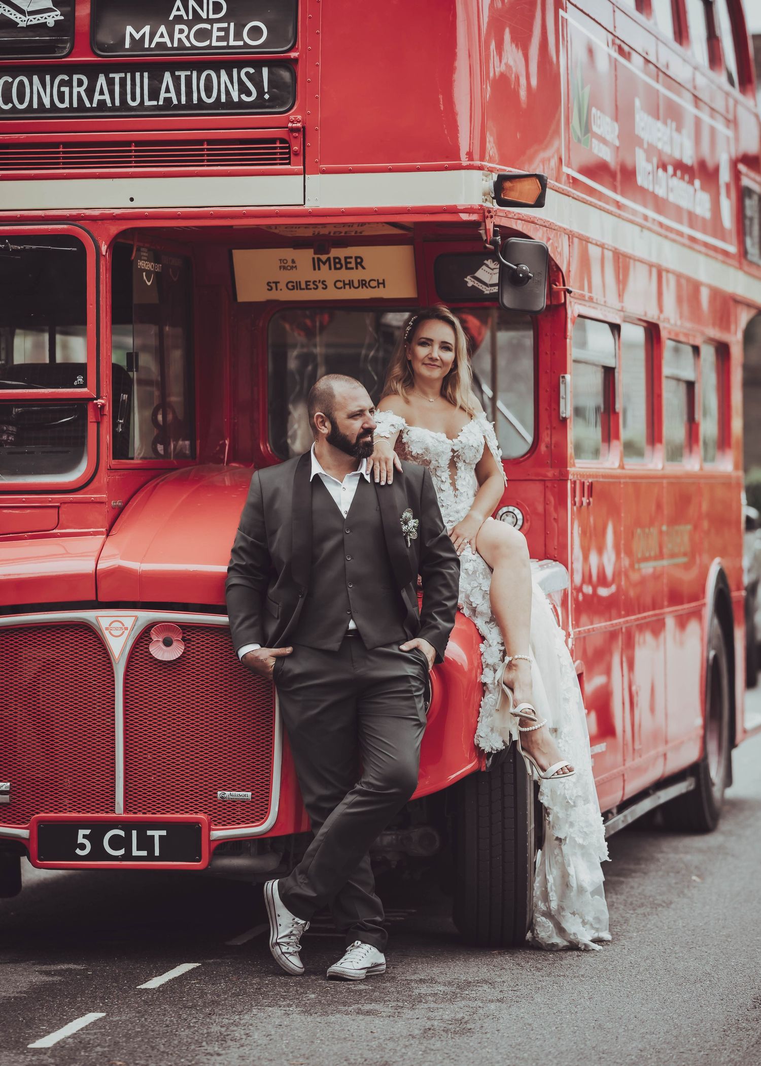 Couple posing by vintage red London bus for wedding photos.