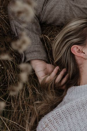 Close-up portrait of couple laying in dried grass wearing cozy sweaters.