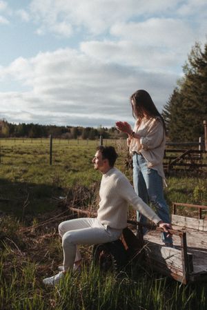 A couple sharing a playful moment on a wooden platform in a rural setting with cloudy skies.