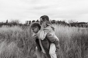 Couple embraces playfully in a field of tall grass on an overcast day.