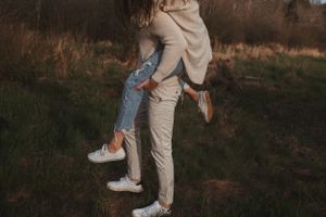 A close-up shot of legs in jeans and beige pants embracing outdoors at sunset.