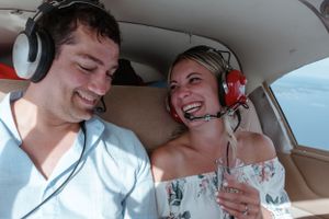 Two people wearing aviation headsets share a laugh inside a small aircraft.