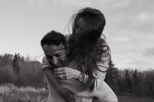 A playful piggyback ride captured in black and white against a scenic forest backdrop.