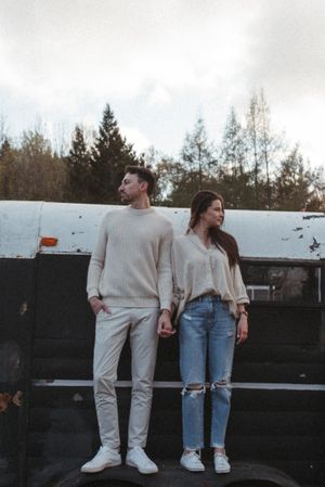 A stylish couple in coordinating neutral outfits standing on a dark surface outdoors.