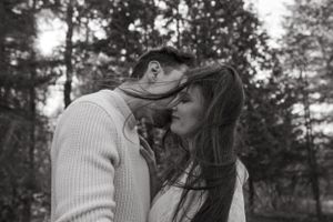 A romantic couple embraces in the woods captured in black and white photography.