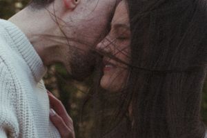 Intimate close-up portrait of couple in white clothing against forest backdrop.