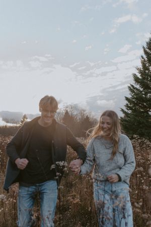A couple walks hand in hand through a field of dried flowers on a cloudy day.