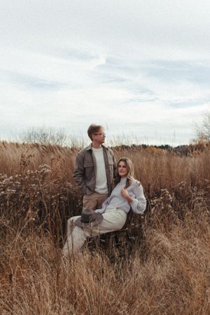 A couple in casual winter wear poses together in a rustic field setting.