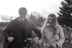 A black and white capture of a couple picking wildflowers together in a field.