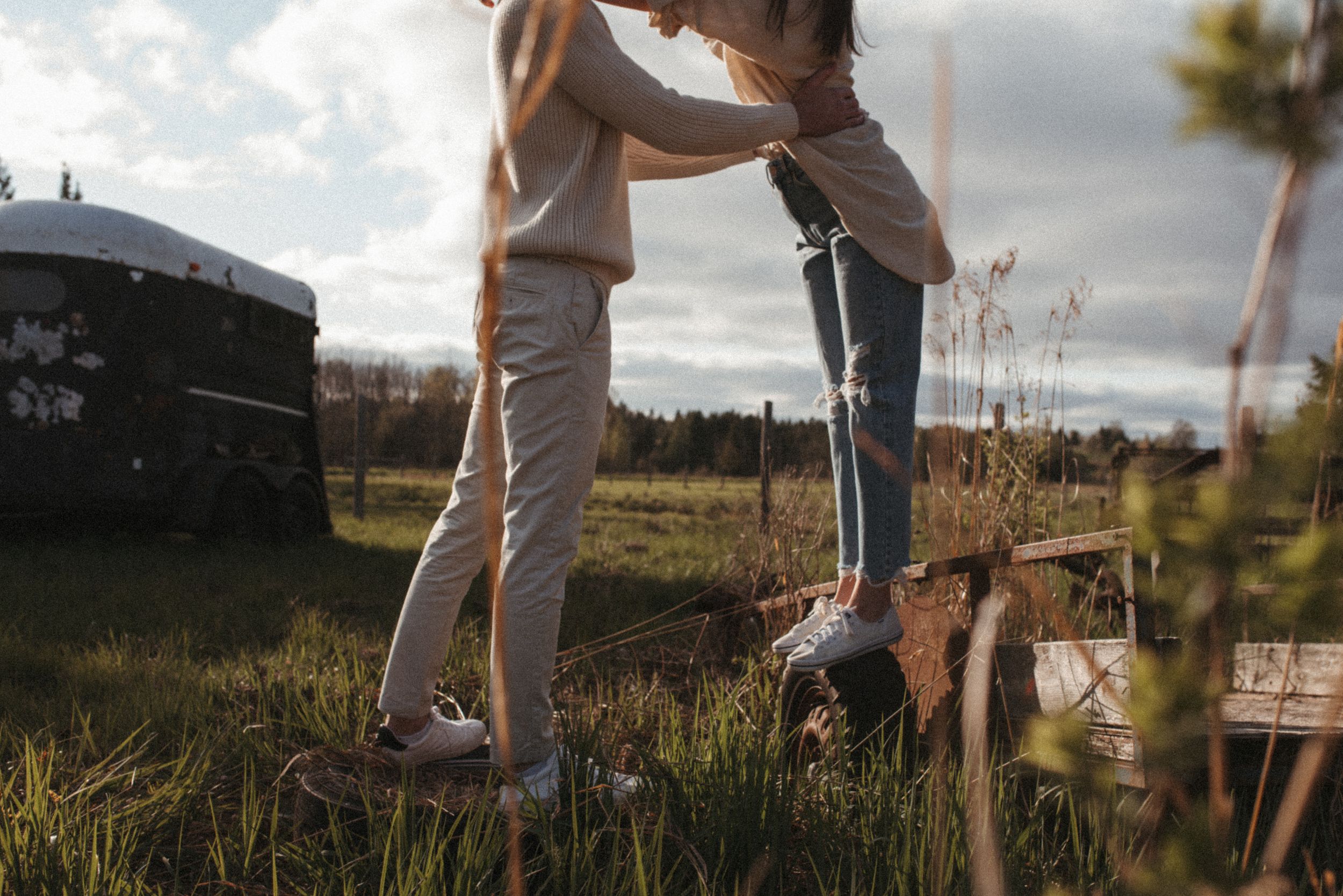 A candid shot of two people's legs standing together in a grassy field at sunset.