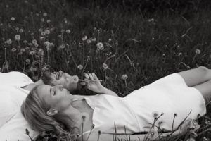 Person in white dress lying among dandelions in black and white.