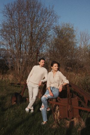 A couple in matching light-colored outfits posing on vintage farm equipment during golden hour.