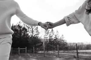 A black and white image showing two people holding hands against a rustic outdoor backdrop.