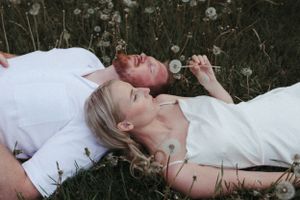 Two people lying in a field of dandelions wearing white clothing.