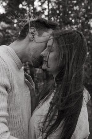 Close up black and white portrait of couple in white sweaters sharing tender moment in forest.