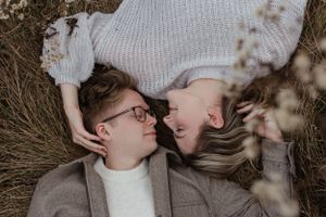 Overhead view of couple lying in dried grass field on cloudy day.