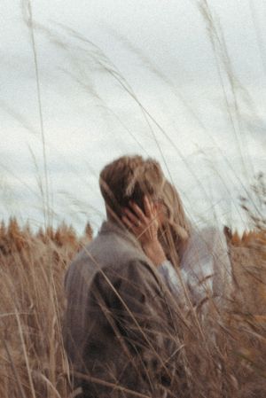 A figure in a brown jacket stands among swaying tall grass.