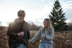 A couple shares laughter while walking through a sunny field with dried wildflowers.